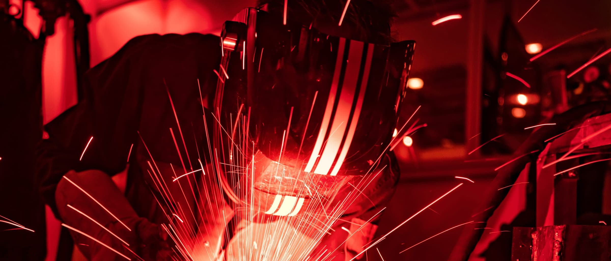 Welder working on steel, sparks lighting a dark fabrication floor